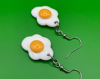 May include: A pair of white and yellow fried egg earrings with silver hooks.