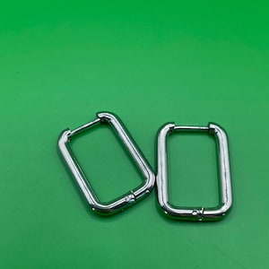 Peut inclure: Une paire de boucles d'oreilles créoles argentées de forme rectangulaire. Les boucles d'oreilles sont simples et modernes.