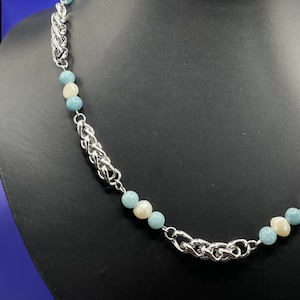 May include: A silver chain necklace with alternating light blue and white beads. The chain is a braided design.