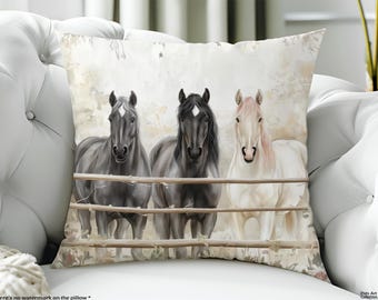 May include: A square throw pillow featuring a printed illustration of three horses standing behind a wooden fence. Two horses are dark gray with white forehead markings, and one horse is white with a light mane. The background has a soft, muted, and light-colored watercolor-style wash.
