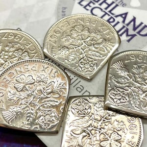 May include: Five silver-coloured coins, each cut into a semi-circular shape, featuring the embossed text SIX PENCE 1967 and floral designs including a rose, thistle, and shamrock. The coins are arranged in a cluster, showing metallic surfaces.