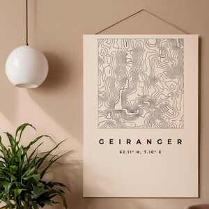 Könnte beinhalten: Beige Wandkunstdruck mit einer topografischen Karte von Geiranger, Norwegen, mit schwarzen Konturlinien. Der Druck enthält den Namen "GEIRANGER" und Koordinaten. Eine weiße Kugelleuchte hängt über einer grünen Pflanze.