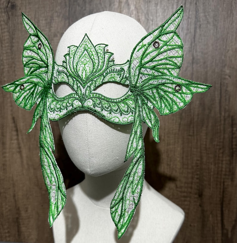 May include: Green masquerade mask with butterfly wings and intricate floral details. The mask is made of lace and has a delicate, feminine design.
