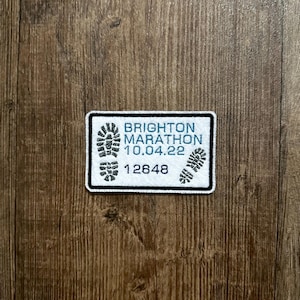May include: White patch with black trim, featuring the text "Brighton Marathon 10.04.22" and the number "12648". Two black footprints are on either side of the text.