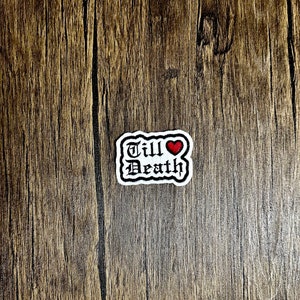 May include: White embroidered patch with black lettering that reads "Till Death" with a red heart above the word "Death".