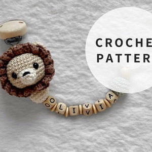 Puede incluir: Patrón de crochet para un juguete de bebé con temática de león con un clip de madera y cuentas que deletrean el nombre "Olivia".