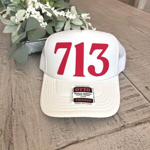 May include: A white trucker hat with the number "713" in red block letters. The hat has a white mesh back and a curved brim. The hat has a "World Famous Foam Front" tag.