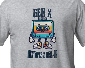 Puede incluir: Camiseta gris con un diseño de casete de cinta de dibujos animados. La cinta tiene una cara sonriente y dice "Gen X Raised on Mixtapes & Dial-Up".