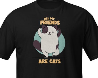 May include: Black t-shirt featuring a cartoon cat illustration. The cat is white with brown spots and a purple tail, standing in front of a teal circle. Text above the cat reads "ALL MY FRIENDS", and below reads "ARE CATS".