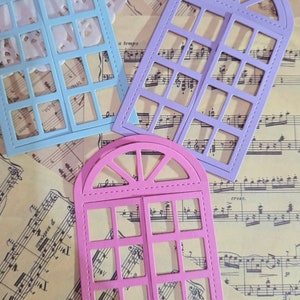 Puede incluir: Tres formas de marco de ventana troqueladas en azul, morado y rosa. Cada marco tiene una parte superior redondeada y una cuadr&iacute;cula de cuadrados. Los marcos est&aacute;n sobre un fondo de partituras musicales.