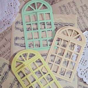 Puede incluir: Tres troqueles en forma de ventana en diferentes colores. Los troqueles est&aacute;n hechos de papel y tienen un dise&ntilde;o decorativo. Los troqueles est&aacute;n sobre un fondo de partituras musicales.