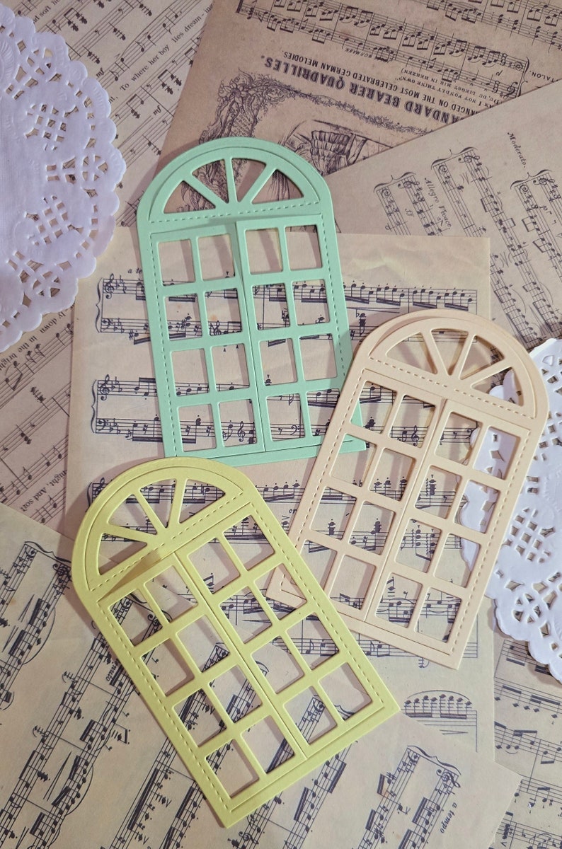 Puede incluir: Tres troqueles en forma de ventana en diferentes colores. Los troqueles est&aacute;n hechos de papel y tienen un dise&ntilde;o decorativo. Los troqueles est&aacute;n sobre un fondo de partituras musicales.