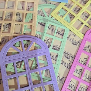Puede incluir: Cinco troqueles de marco de ventana de diferentes colores, cada uno con un dise&ntilde;o diferente. Los troqueles est&aacute;n dispuestos en una hoja de papel de m&uacute;sica. Los colores son morado, verde, amarillo, azul y rosa.