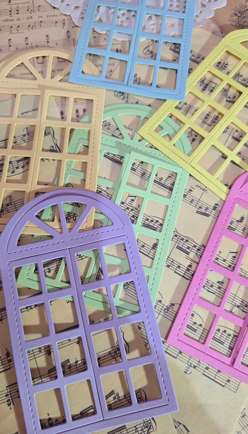Puede incluir: Cinco troqueles de marco de ventana de diferentes colores, cada uno con un dise&ntilde;o diferente. Los troqueles est&aacute;n dispuestos en una hoja de papel de m&uacute;sica. Los colores son morado, verde, amarillo, azul y rosa.
