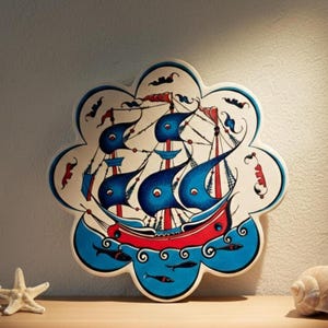 Può includere: Un piatto decorativo in ceramica a tema nautico. Il piatto presenta una nave stilizzata con vele blu e scafo rosso, su sfondo bianco. Il piatto ha un bordo smerlato unico ed è decorato con motivi di pesci e onde.