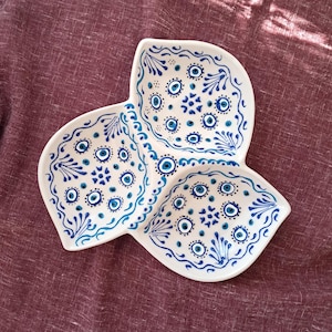 Könnte beinhalten: Eine weiße Keramik-Servierplatte mit drei Abschnitten. Jeder Abschnitt ist mit einem blauen und weißen Muster aus bösen Augen-Symbolen und floralen Designs verziert.