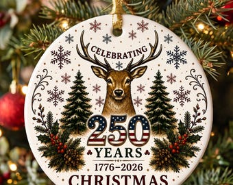 May include: A round white ceramic ornament featuring a brown deer head, two green pine trees, and red holly berries. The text reads CELEBRATING 250 YEARS 1776-2026 CHRISTMAS. The number 250 is filled with a red, white, and blue American flag pattern.
