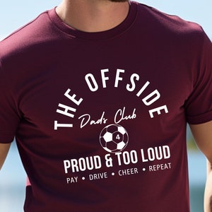 Op de afbeelding: Bordeauxkleurig T-shirt met een witte afbeelding van een voetbal en de tekst "The Offside Dad's Club - Proud & Too Loud - Pay Drive Cheer Repeat"