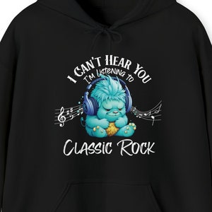 Op de afbeelding: Zwarte hoodie met een afbeelding op de voorkant. De afbeelding toont een blauw, harig wezen met een koptelefoon, met muzieknoten en de tekst "I CAN'T HEAR YOU I'M LISTENING TO CLASSIC ROCK."