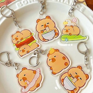 May include: Set of seven clear acrylic keychains featuring cartoon bears in various poses. Each keychain has a metal ring and a different bear design. The bears are eating ramen, a burger, and other foods.