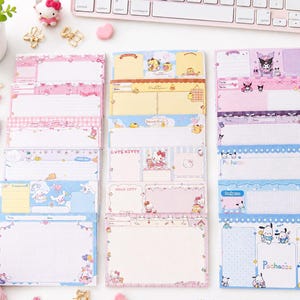May include: A collection of rectangular memo pads featuring Sanrio characters including Hello Kitty, Kuromi, Pompompurin, and Pochacco. The pads are arranged in three vertical columns, displaying various pastel colour schemes, grid patterns, and lined sections.