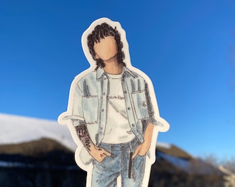 May include: A sticker of a person wearing a blue denim jacket over a white t-shirt with the text "Calvin Klein" on it. The person is wearing blue jeans and has a tattoo on their arm.