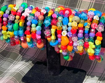 May include: A collection of colorful beaded bracelets. The bracelets feature a variety of shapes, including flowers, hearts, and stars, in shades of red, orange, yellow, green, blue, and purple. The bracelets are displayed on a black stand.