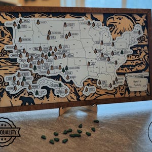 May include: Wooden map of the United States with laser-cut details, including state outlines, tree markers, and a bear silhouette. The map is framed in dark wood and includes the text "Byer's Family".