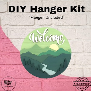 May include: DIY Hanger Kit with the text "Welcome" in white script over a layered mountain and river scene. The kit includes a hanger. The design features shades of green and a yellow sun. The words "Made in USA" and "High Quality" are also visible.