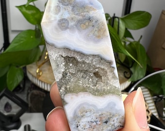 May include: White, gray, and brown agate crystal point with a clear quartz druzy center. The crystal is polished and has a smooth, rounded shape.