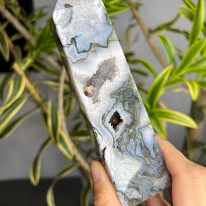 Può includere: Una punta di cristallo di agata grigia e verde con una formazione naturale di druse e un piccolo cristallo verde in cima. Il cristallo è levigato e ha una superficie liscia.