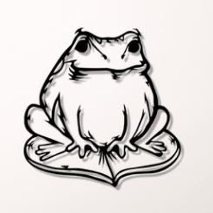 以下が含まれることがあります： 蓮の葉に座っているカエルの黒い金属製の壁飾り。カエルはシンプルなデザインでスタイリッシュに描かれており、笑顔をしています。