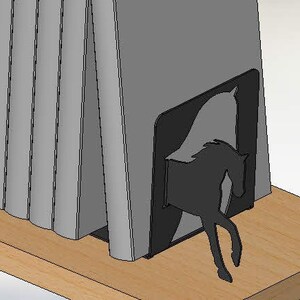 Pode incluir: Uma caixa retangular coberta de tecido cinza com uma silhueta de cavalo preto espiando pela abertura. A caixa está sobre uma superfície de madeira.