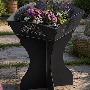 Puede incluir: Una jardinera de metal negro con un diseño decorativo recortado, llena de vibrantes flores moradas, rosas y blancas. La jardinera tiene una base única ensanchada y está colocada sobre un patio de piedra en un jardín.