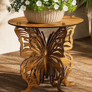 May include: A wooden butterfly-shaped side table with a round top, holding a pot of white and purple flowers. The table has a natural wood finish and is placed on a wooden floor. A large potted plant is in the background.