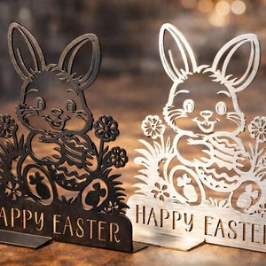 May include: Two laser-cut Easter bunny decorations. One is dark brown, the other is light brown. Each bunny is surrounded by floral and grass cutouts, and the words "HAPPY EASTER" are at the base of each decoration.