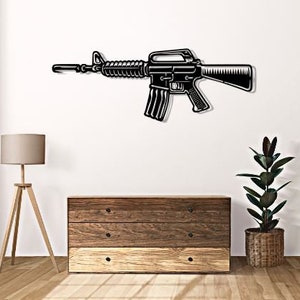 Puede incluir: Arte de pared de metal negro que representa un rifle con culata de madera y cañón negro. El rifle está montado en una pared blanca sobre una cómoda de madera con tres cajones.