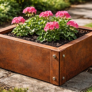 Op de afbeelding: Een rechthoekige metalen plantenbak met een verweerde, roestige uitstraling, gevuld met aarde en felroze geraniums. De bak, vastgezet met bouten, staat op een stenen oppervlak. Het ontwerp is rustiek, met afmetingen van ongeveer 60 cm x 30 cm x 30 cm.