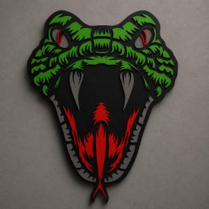 Peut inclure: Une décoration murale en couches représentant une tête de serpent stylisée avec la gueule ouverte. Le design présente une base noire avec des écailles vert vif, des yeux rouges, des crocs gris et une langue fourchue rouge au centre.
