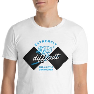 May include: White t-shirt with a graphic design featuring a skier in blue and the words "EXTREMELY difficult AND A LITTLE UNGROOMED" in a black diamond shape. The shirt is made of a soft material.
