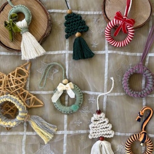 May include: A collection of handmade Christmas decorations featuring various designs, including wreaths, stars, and trees. The decorations are made with yarn and have a variety of colours, including green, red, white, and purple.