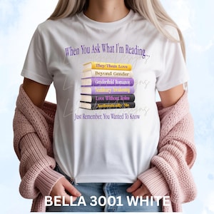 May include: White t-shirt with the text "When You Ask What I'm Reading..." and a stack of books. Each book has a title, including "They Them Love" and "Beyond Gender." The shirt also says "Just Remember, You Wanted To Know."