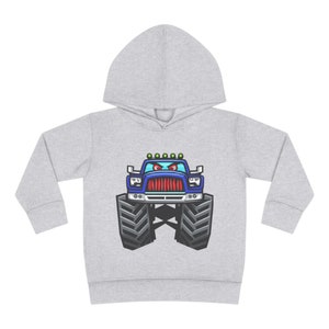 May include: A gray hooded sweatshirt with a cartoon monster truck design. The truck is blue with red eyes and a black grill. The truck has large tires and is driving on a dirt road.