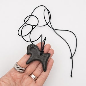 May include: A black horse pendant necklace. The pendant is a stylized horse shape with a textured surface, suspended from a black cord. The necklace is shown against a white background.