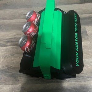 Pode incluir: Uma caixa de isopor preta e verde para seis latas com al&ccedil;a. A caixa de isopor tem espa&ccedil;o para seis latas e o texto "YOUR CUSTOM TEXT HERE" est&aacute; impresso no lado.