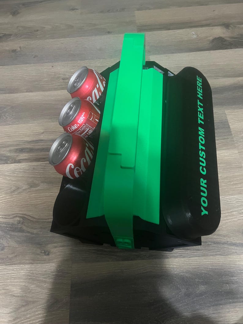 Pode incluir: Uma caixa de isopor preta e verde para seis latas com al&ccedil;a. A caixa de isopor tem espa&ccedil;o para seis latas e o texto "YOUR CUSTOM TEXT HERE" est&aacute; impresso no lado.