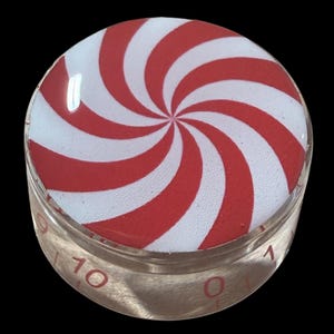 Puede incluir: Perilla redonda y transparente con un diseño de remolino rojo y blanco de menta. La perilla tiene una escala del 0 al 10. El diseño recuerda a un bastón de caramelo clásico.
