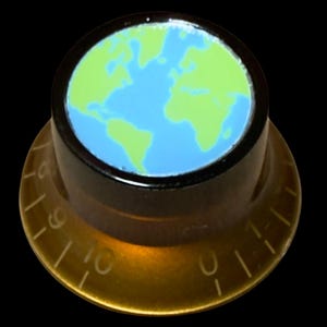 May include: A cylindrical control knob with a black top featuring a light blue and lime green map of the world. The base is a translucent amber-colored plastic with white numerical markings from zero to ten etched around the outer edge.