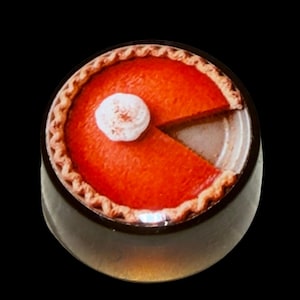 Peut inclure: Une tarte à la citrouille orange ronde avec un bord de croûte cannelé, surmontée d'une seule noisette de crème fouettée blanche. Une part triangulaire a été retirée de la tarte, révélant la surface métallique du moule sous la garniture.