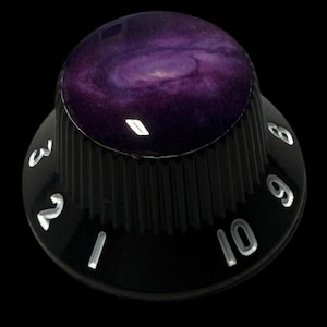 May include: A black guitar knob with a galaxy design on top. The knob has white numbers from 1 to 10 and is set against a black background. The galaxy design features shades of purple and white.